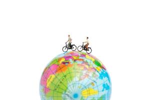 Viajeros en miniatura con bicicletas en un globo terráqueo sobre un fondo blanco. foto