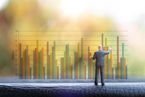 Miniature businessman standing in front of a graph chart background photo