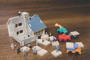 Miniature workers repairing a house on a wooden background photo