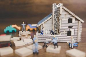 Miniature workers repairing a house on a wooden background photo