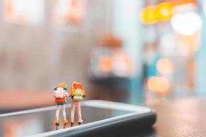Miniature backpacker tourist people standing on a smartphone, travel concept photo