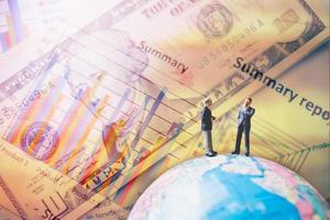 Miniature businessmen standing on a globe world map with a graph and banknotes in the background photo