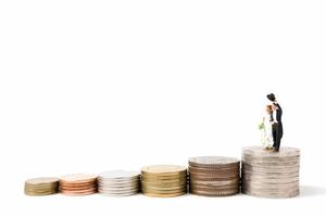 Miniature wedding, bride and groom on a stack of coins on a white background photo