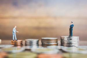 Miniature businesspeople standing on money with a wooden background photo