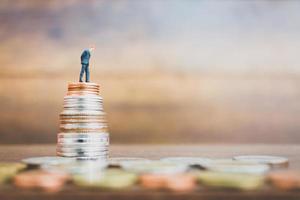 Miniature businessman standing on money with a wooden background photo