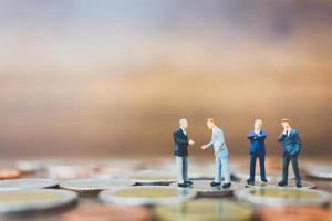 Miniature businesspeople standing on money with a wooden background photo