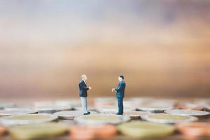 Miniature businesspeople standing on money with a wooden background photo