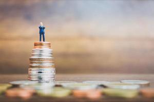 Miniature businessman standing on money with a wooden background