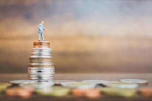 Miniature businessman standing on money with a wooden background photo