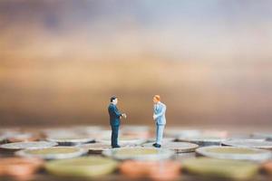 Miniature businesspeople standing on money with a wooden background photo