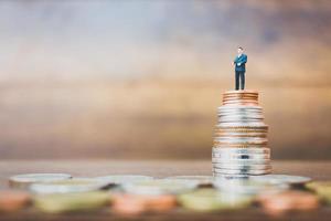 Miniature businessman standing on money with a wooden background photo