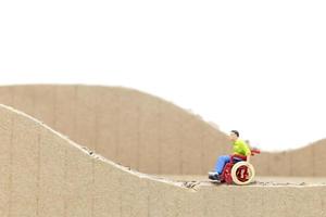 Miniature man in a wheelchair on a cardboard cutout isolated on a white background photo