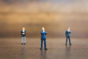 Miniature businesspeople standing on a wooden background photo