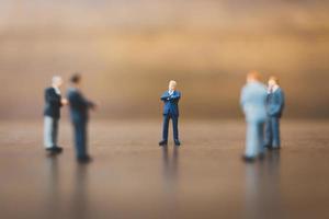 Miniature businesspeople standing on a wooden background photo