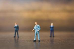 Miniature businesspeople standing on a wooden background photo