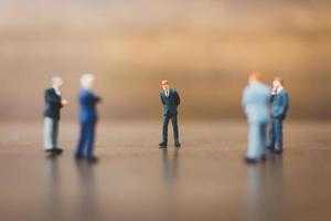 Miniature businesspeople standing on a wooden background photo