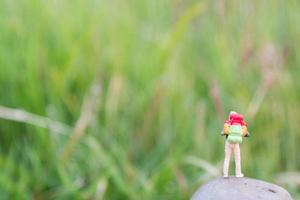 Viajero en miniatura con una mochila de pie y caminando en un prado foto