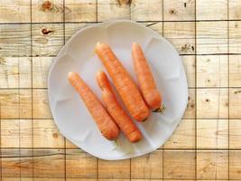 Zanahorias en un plato blanco sobre un fondo de mesa de madera foto