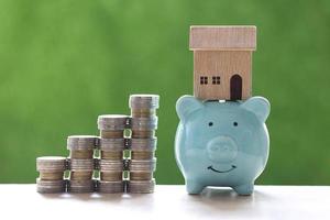 Stack of coins next to a piggy bank with a model house on a natural green background photo