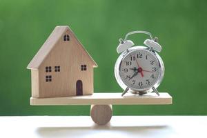 Retro alarm clock and model house on a wood scale on a natural green background, business investment and real estate concept photo