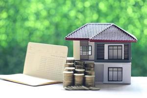 Model house and a stack of coins with a banking account book on a natural green background, business investment and real estate concept photo