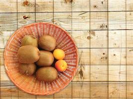 Kiwis y albaricoques en una cesta de mimbre sobre un fondo de mesa de madera foto