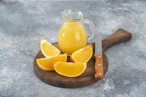 Orange slices with a glass pitcher of fresh juice placed on a wooden round board photo