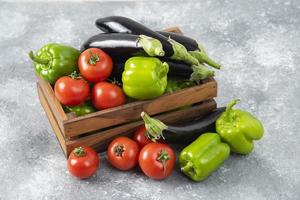 Wooden box full of fresh ripe vegetables placed on a stone background