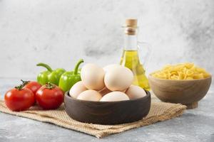 huevos de gallina crudos con una botella de vidrio de aceite y verduras frescas foto