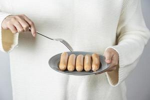 Female hands holding a plate of boiled sausages against a gray wall photo