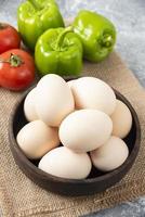 Recipiente de madera lleno de huevos de gallina cruda con verduras frescas maduras en un cilicio foto