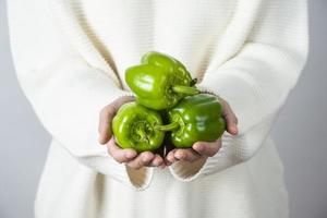 Female hands holding a heap of green bell peppers against a gray wall photo