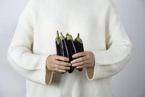 Female hands holding ripe eggplant vegetables against a gray wall photo