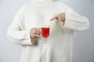 Female hands holding and pointing at a glass cup of tomato juice against a gray wall photo