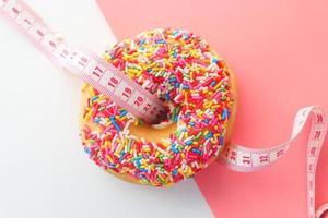 Cerca de donut con una cinta métrica sobre fondo de color rosa foto
