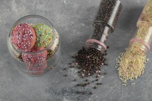 Two bottles of colorful sprinkle dotes and a jar of doughnuts on a marble background photo