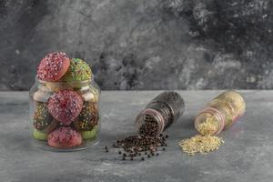 Two bottles of colorful sprinkle dotes and a jar of doughnuts on a marble background photo