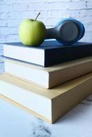 Stack of books, apple, and headphones on table photo
