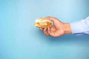 Hand holding a sandwich against blue background with copy space