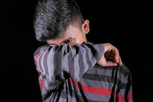 Man sneezing into elbow on black background photo