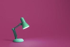 Retro green desk lamp turned on and bent over shining on a bright pink background photo