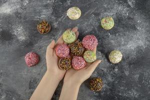 manos sosteniendo coloridos dulces pequeños donuts con chispitas foto
