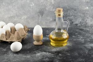 Huevo de gallina crudo en una huevera con una huevera y un vaso de aceite sobre un fondo de mármol