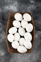 Un mimbre de madera lleno de huevos de gallina crudos blancos. foto