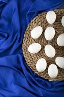 White raw chicken eggs on a wooden piece on blue cloth