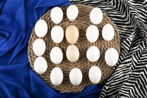 Brown and white raw chicken eggs on a wooden piece on blue cloth photo