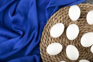White raw chicken eggs on a wooden piece on blue cloth