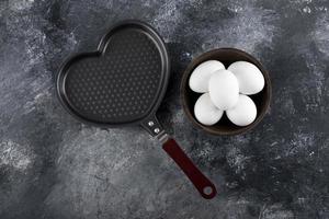 Bowl of white eggs next to a heart-shaped pan photo