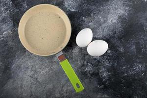 huevos blancos crudos junto a una sartén vacía foto