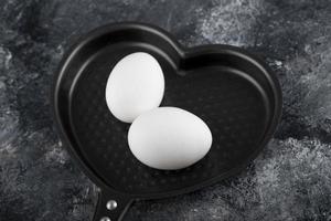 dos huevos blancos en una sartén en forma de corazón foto